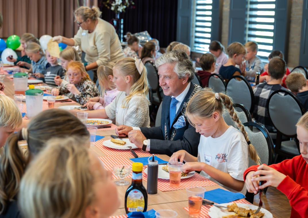 Burgemeester Beenakker met kinderen aan tafel tijdens de pannenkoekenmiddag.