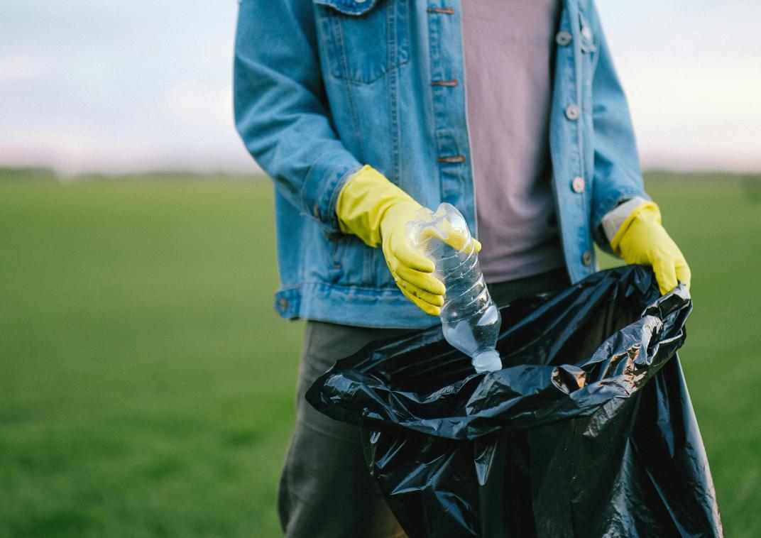 Persoon stopt plastic fles in een afvalzak.