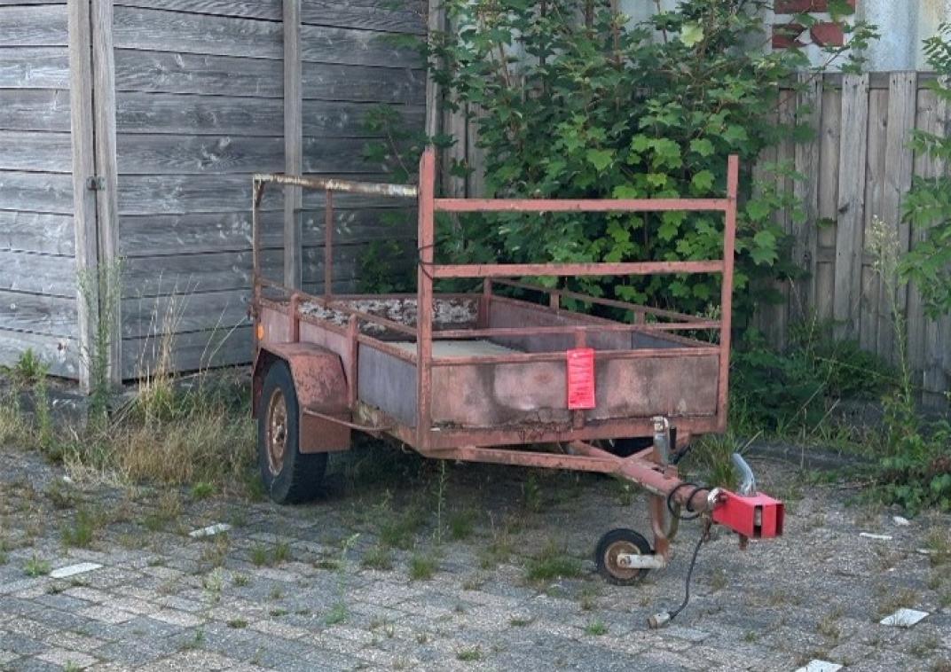 Bruine, roestige aanhanger naast een houten schutting